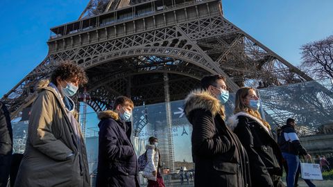 Menschen mit Masken laufen in Paris am Eiffelturm vorbei