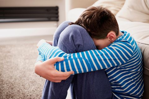 Trauriger Junge umarmt die Knie auf dem Sofa im Wohnzimmer