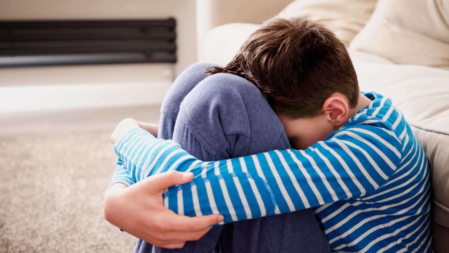Trauriger Junge umarmt die Knie auf dem Sofa im Wohnzimmer