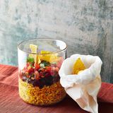 Burrito-Schicht-Salat      Zutaten:  250 g Naturreis (ersatzweise »Dinkel wie Reis«), 1 Bio-Limette (ersatzweise BioZitrone), 500 g Tomaten, 1 Bund Schnittlauch, 3 EL Ahornsirup, Salz, Pfeffer, 1 Zwiebel, 1 Dose schwarze Bohnen, (240 g Abtropfgewicht, ersatzweise Kidneybohnen), 1 EL neutrales Pflanzenöl, 1 EL Tomatenmark, ¼ TL gemahlener Kreuzkümmel, ¼ TL gemahlener Koriander, 2 Msp. Cayennepfeffer, ½ TL gemahlene Kurkuma, 2 EL Weißwein- oder Apfelessig, 2 TL geröstetes Sesamöl, ½ Bund Koriander, 3 Handvoll Tortillachips      Zubereitung:  1. Den Reis in ein feines Sieb geben und mit kaltem Wasser abwa - schen, bis das Wasser klar bleibt. Dann in der doppelten Menge Wasser nach Packungsanweisung garen.  2. Für die Salsa die Limette heiß abwaschen, trocken tupfen, die Schale abreiben und den Saft auspressen. Die Tomaten waschen, vom Stielansatz befreien und entkernen. Das Fruchtfleisch fein würfeln. Den Schnittlauch waschen, trocken schütteln und in feine Röll - chen schneiden. Schnittlauch, 1 EL Ahornsirup und Limettensaft zu den Tomatenwürfeln geben und unterheben, die Salsa mit Salz und Pfeffer abschmecken.  3. Die Zwiebel schälen und würfeln. Die Bohnen durch ein Sieb abgie - ßen und abtropfen lassen. Das Öl in einer Pfanne erhitzen und die Zwiebeln darin goldbraun anbraten. Bohnen und Tomatenmark da - zugeben und unter Rühren 1 Min. anrösten. Kreuzkümmel, Korian - der und Cayennepfeffer dazugeben, umrühren und mit 100 ml Was - ser ablöschen. 30 Sek. köcheln lassen, bis die Sauce eindickt, dann vom Herd ziehen und mit Salz abschmecken.  4. Den Reis mit Kurkuma, Essig, Sesamöl und restlichem Ahornsirup (2 EL) mischen, mit etwas Salz abschmecken und zum Mitnehmen auf 4 Schraubgläser oder Boxen verteilen. Die Bohnen und Tomaten obenauf schichten. Koriander waschen, trocken schütteln und über die Bohnen streuen. Verschließen und kalt stellen. Die Chips ge - trennt verpacken und zum Salat servieren.