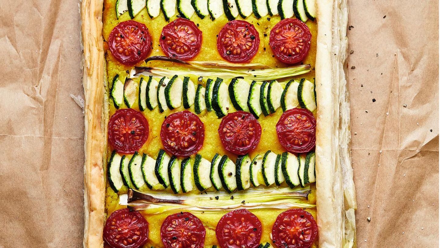 Blätterteigtarte mit Fava und Gemüse      Zutaten:  200 g gelbe Schälerbsen (Fava, ersatzweise gelbe Linsen), 2 Lorbeerblätter, 1 Zwiebel, 2 Knoblauchzehen, 1 kleine Bio-Zitrone, 50–80 ml ungesüßter Pflanzendrink, 4 EL natives Olivenöl, ½ TL gemahlene Kurkuma, Salz, ½ Zucchino, 2 Frühlingszwiebeln, 6 Kirschtomaten, 1 Packung veganer Blätterteig (275 g), schwarzer Pfeffer aus der Mühle      Zubereitung:  1. Die Erbsen 3 Std. in kaltem Wasser einweichen. Das Einweichwasser danach abgießen und die Erbsen mit den Lorbeerblättern in der doppelten Menge Wasser aufkochen. Ohne Deckel in ca. 20 Min. weich kochen (Achtung, es schäumt!).  2. Währenddessen die Zwiebel und den Knoblauch schälen und grob würfeln. Die Zitrone heiß abwaschen, trocknen, die Schale abreiben und 3 EL Saft auspressen. Die Erbsen abgießen, die Lorbeerblätter entfernen. Die weichen Erbsen mit Zwiebeln, Knoblauch, Zitronen - saft, 50 ml Pflanzendrink, Olivenöl, Kurkuma und etwas Salz fein cremig pürieren. Falls nötig, noch etwas mehr Pflanzendrink dazu - geben.  3. Zucchino, Frühlingszwiebeln und Tomaten waschen und abtropfen lassen. Vom Zucchino den Blüten- oder Stielansatz gerade abschnei - den und den Zucchino auf 10 cm Länge kürzen. Dann längs vier - teln, das Kerngehäuse herausschneiden und den Zucchino in 3 mm dicke Scheiben schneiden. Die Frühlingszwiebeln putzen und vom unteren, weißen Teil 10 cm lange Stücke abschneiden, diese vierteln. Die Tomaten halbieren.  4. Den Backofen auf 200° vorheizen. Ein Backblech mit Back - papier auslegen, den Blätterteig darauflegen und zu einer Fläche von 15 × 40 cm schneiden. Die kürzeren Seiten 1,5 cm, die langen Seiten 1 cm nach innen umschlagen und festdrücken. Vom rest - lichen Blätterteig 2 lange und 2 kurze Streifen abschneiden, sodass diese zu den Seitenlängen der Tarte passen.  5. Die Erbsencreme auf das große Blätterteigstück streichen, dabei die Ränder aussparen. Das Gemüse auf der Creme verteilen. Die Ränder der Tarte mit Wasser bestreichen, die übrigen Teigstreifen darauflegen und leicht andrücken. Die Tarte im Backofen (Mitte) 15 Min. backen, bis die Ränder der Tarte leicht gebräunt sind. Aus dem Ofen nehmen, mit etwas Salz und gemahlenem schwarzen Pfeffer aus der Mühle bestreuen. Dazu passt ein grüner Salat.
