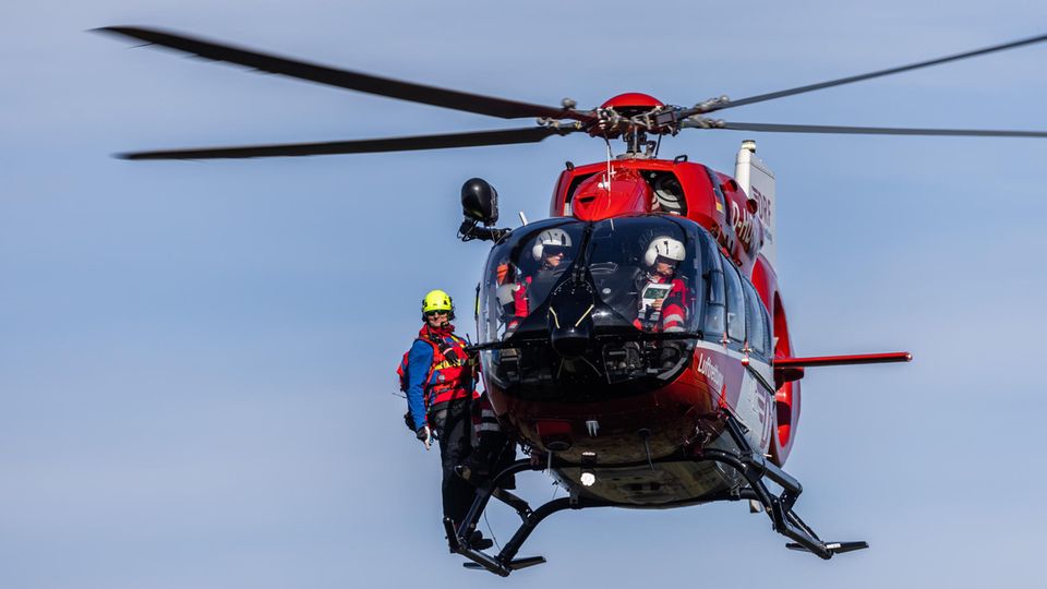 Im Einsatz: Ein Mitglied der Bergwacht steht auf den Kufen eines Hubschraubers, der mit einer Winde ausgestattet ist, um Verunglückte zu retten.