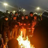 Menschen, die an einer Kundgebung teilnehmen und sich an einem Feuer wärmen.