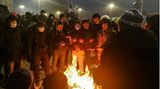 Menschen, die an einer Kundgebung teilnehmen und sich an einem Feuer wärmen.