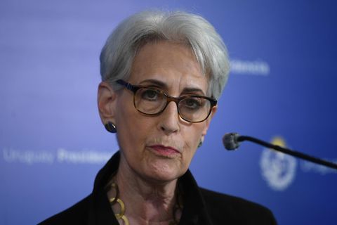 Eine älter weiße Frau mit kurzen, grau-weißen Haaren und Hornbrille hört einer Frage zu