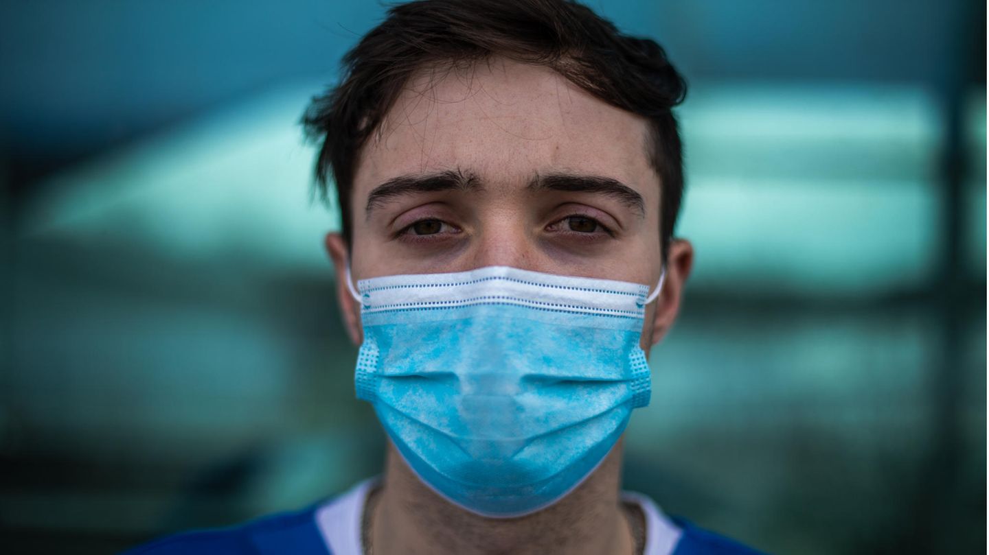 Junger Mann mit OP-Maske schaut mit erschöpften Augen in die Kamera