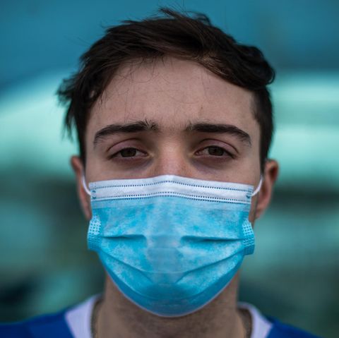 Junger Mann mit OP-Maske schaut mit erschöpften Augen in die Kamera