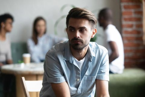 Junger Mann sitzt alleine und eingeschüchtert in einem Café