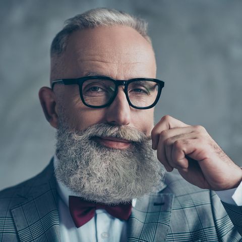 Ein älterer Mann mit grauem Haar und langem Bart lächelt verschmitzt