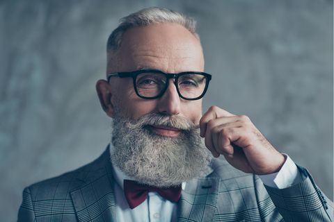 Ein älterer Mann mit grauem Haar und langem Bart lächelt verschmitzt