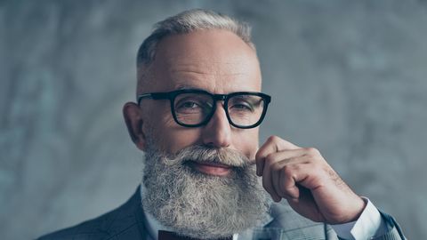 Ein älterer Mann mit grauem Haar und langem Bart lächelt verschmitzt