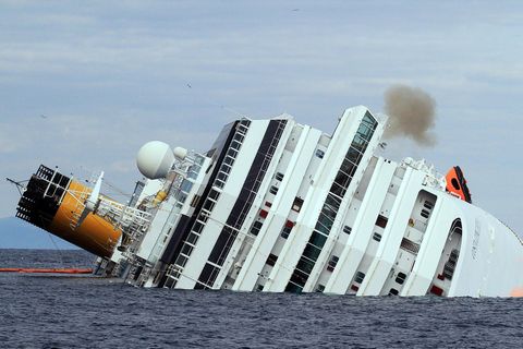 Ein weißes Kreuzfahrtschiff liegt mit Schlagseite im Meer. Auf der einen Seite hängen noch orangene Rettungsinseln