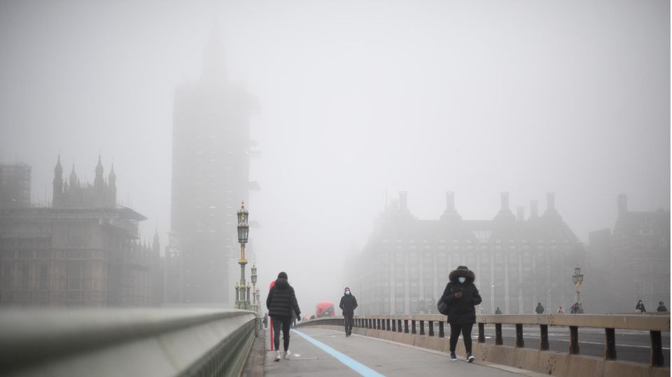 Passanten auf einer Brücke in London, die Luft wirkt neblig