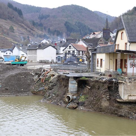 Über einem grün-braunen Flüsschen steht die Ruine eines Hauses, das bei der Flut im Ahrtal beschädigt wurde