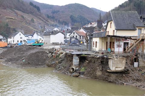 Über einem grün-braunen Flüsschen steht die Ruine eines Hauses, das bei der Flut im Ahrtal beschädigt wurde
