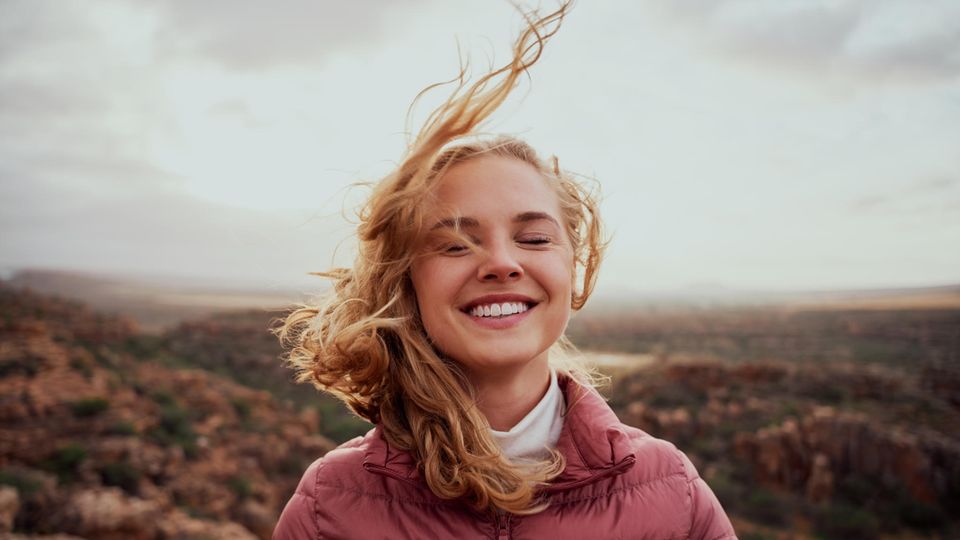 Eine junge Frau lächelt während der Wind ihr die Haare um den Kopf bläst