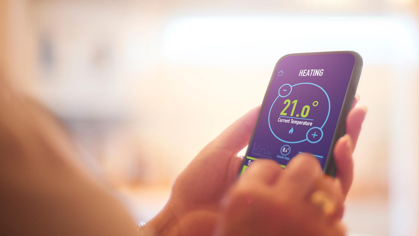 Smart-Thermostat: Eine Frau stellt an ihrem Smartphone per App die Heizung ein.