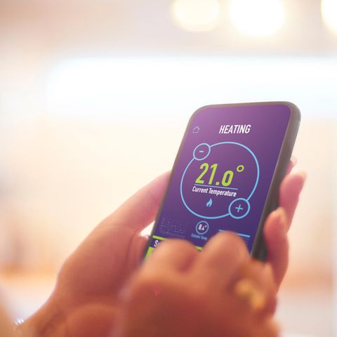 Smart-Thermostat: Eine Frau stellt an ihrem Smartphone per App die Heizung ein.