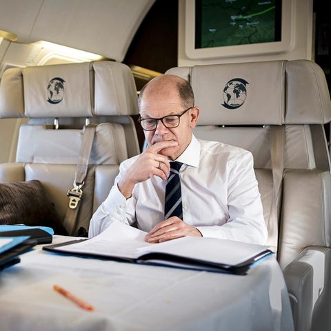 Olaf Scholz geht in einem Flugzeug Unterlagen durch