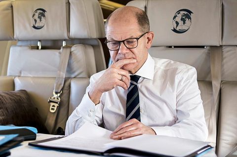 Olaf Scholz geht in einem Flugzeug Unterlagen durch