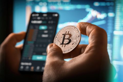 Eine Person hält einen Bitcoin in der Hand und tätigt einen Handel mit Kryptowährungen
