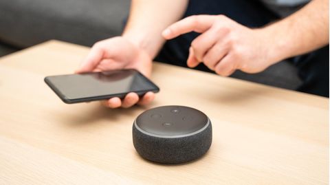 Der Echo Dot steht auf einem Tisch und wird mit dem Smartphone gesteuert.