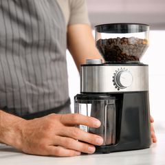 Mann mit elektrischer Kaffeemühle in der Küche