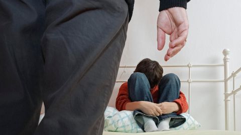 Sexueller Missbrauch: Ein Mann steht vor einem Bett, auf dem ein zusammengekauerter Junge sitzt