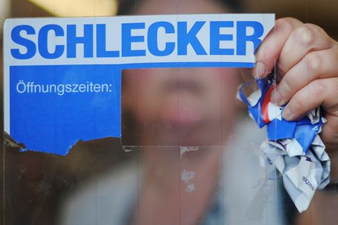 Mitarbeiterin reißt Schlecker-Sticker von einem Fenster.