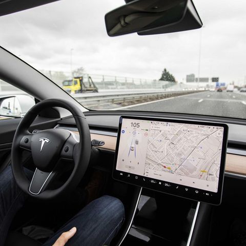 Ein Mann sitzt am Steuer eines Tesla-Autos und hat seine Hände während der Fahrt nicht am Lenkrad.