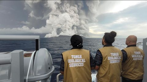 Drei Personen schauen sich den Vulkanausbruch von der Ferne an