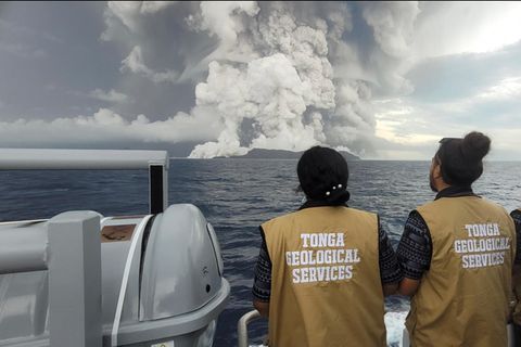 Drei Personen schauen sich den Vulkanausbruch von der Ferne an