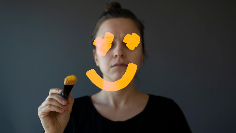 Eine Frau malt auf den Spiegel ein Smiley, der ihr Gesicht verdeckt