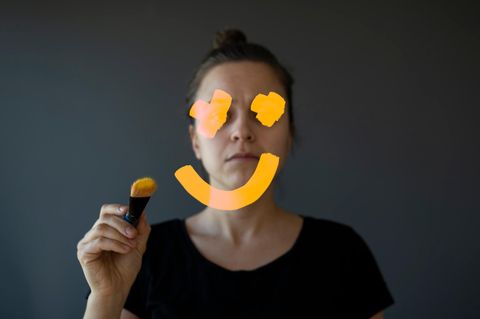 Eine Frau malt auf den Spiegel ein Smiley, der ihr Gesicht verdeckt