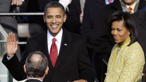 Barack Obama hält eine Hand auf eine Bibel und die andere Hand in die Höhe. Neben ihm steht seine Frau Michelle