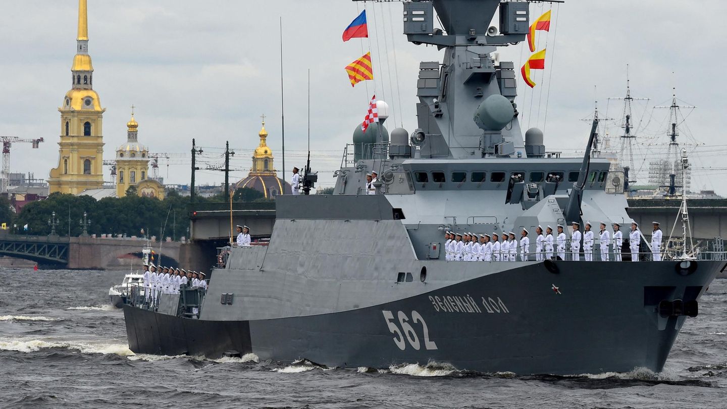 An Deck eines grauen Kriegsschiffes mit kyrillischer Schrift und der Nummer 562 am Bug stehen Soldaten in weißen Uniformen