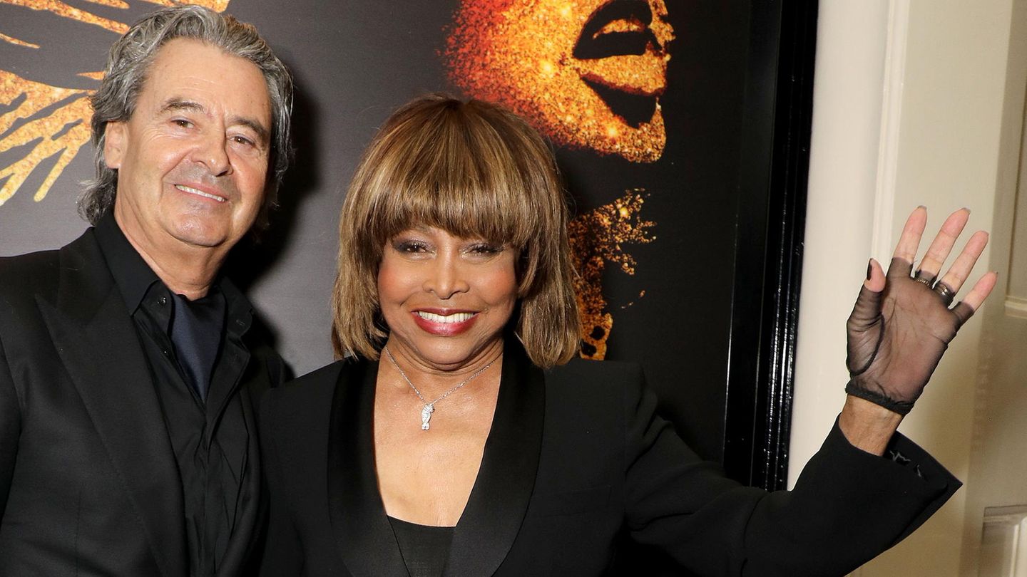 Tina Turner und Erwin Bach bei einer Veranstaltung. Sie tragen Schwarz und sie winkt