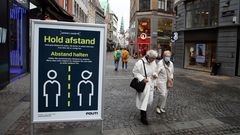 "Hold afstand" und "Abstand halten" steht auf einem Schild in einer Straße in Kopenhagen. Zwei weißhaarige Damen gehen vorbei