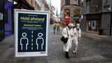 "Hold afstand" und "Abstand halten" steht auf einem Schild in einer Straße in Kopenhagen. Zwei weißhaarige Damen gehen vorbei