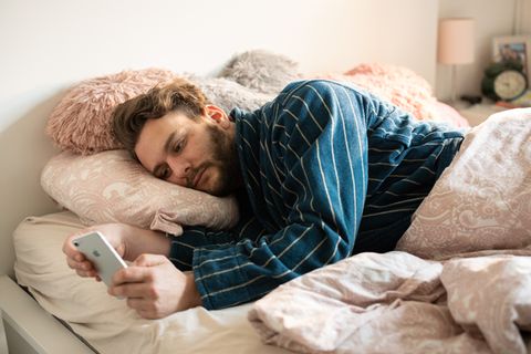Benedikt Herber liegt mit seinem Handy in der Hand im Bett