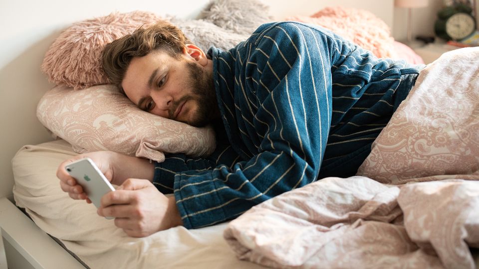Benedikt Herber liegt mit seinem Handy in der Hand im Bett