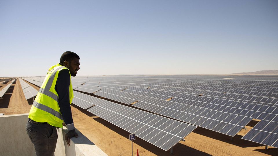 Ein Arbeiter schaut auf eine Photovoltaik-Freiflächenanlage in der ägyptischen Wüste bei Aswan