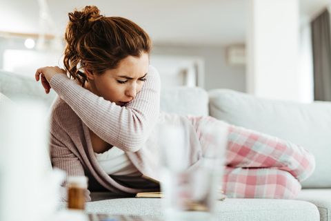Omikron Symptome Risiko: Eine Frau hustet in den Ellenbogen