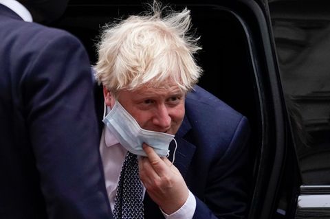 Ein weißer Mann mit strubbeligen weiß-blonden Haaren steigt in Anzug und Krawatte aus einem Auto