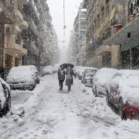 Menschen gehen in Athen bei Schneefall durch eine Straße
