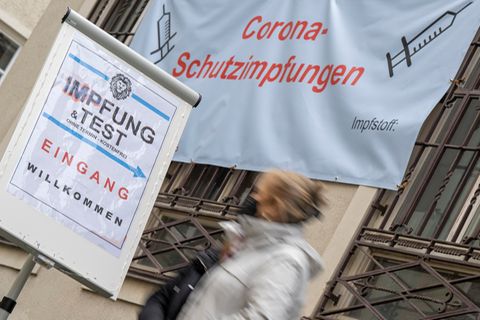 Impfpflicht-Debatte: Frau geht unter Plakat mit Aufschrift Corona-Impfung