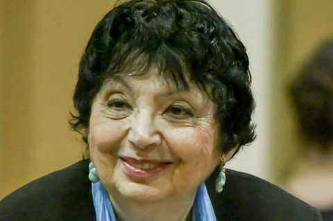 Eine ältere Frau dunklen, kurzen Haaren, Ohrringen und einem blauen Schal