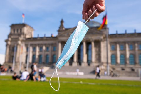 Eine Hand hält eine Maske vor dem Reichstag