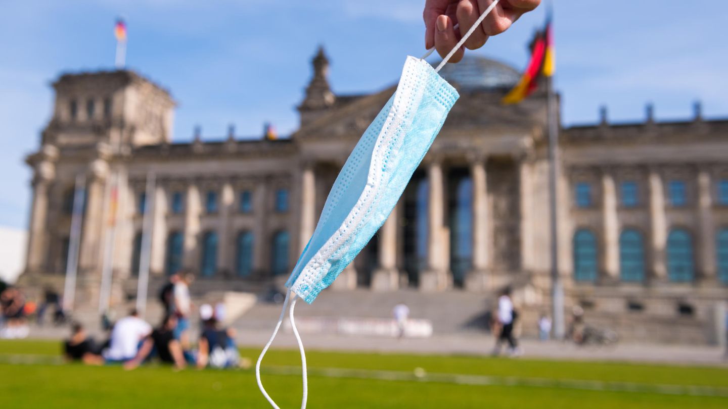 Eine Hand hält eine Maske vor dem Reichstag