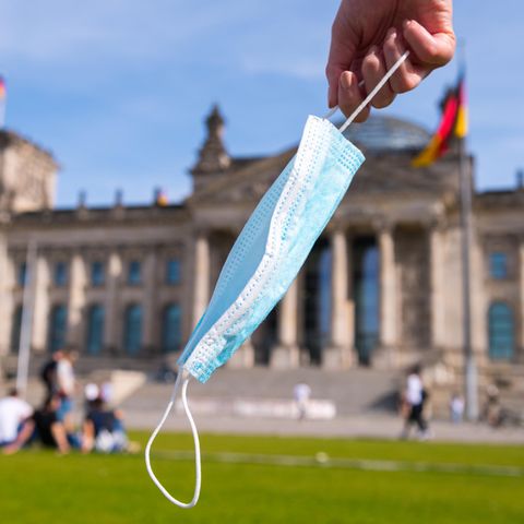 Eine Hand hält eine Maske vor dem Reichstag